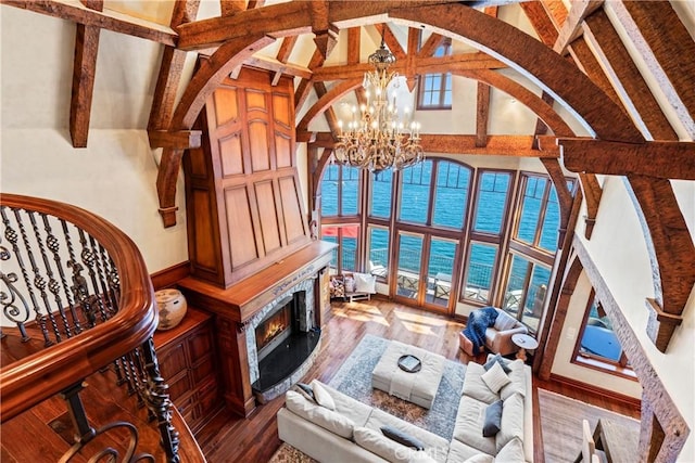 living room featuring hardwood / wood-style floors, beam ceiling, a premium fireplace, an inviting chandelier, and a water view