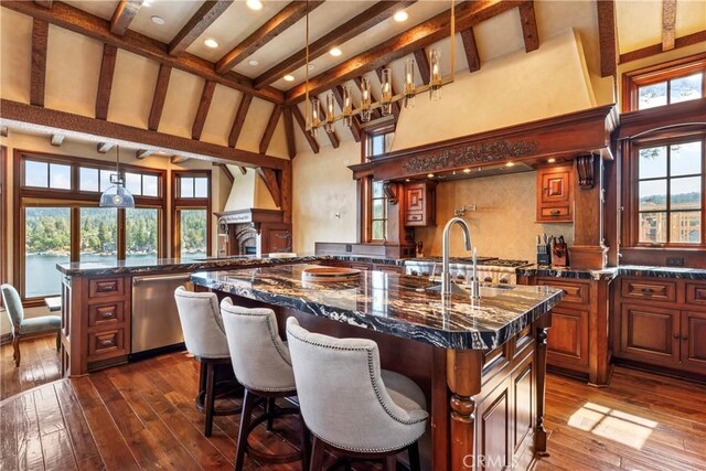 kitchen with dishwasher, a large island with sink, sink, hanging light fixtures, and dark stone counters