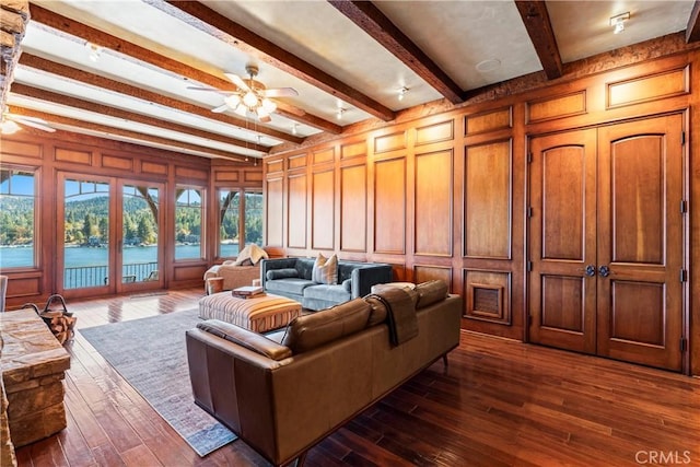 living room featuring ceiling fan, dark hardwood / wood-style floors, beamed ceiling, a water view, and french doors