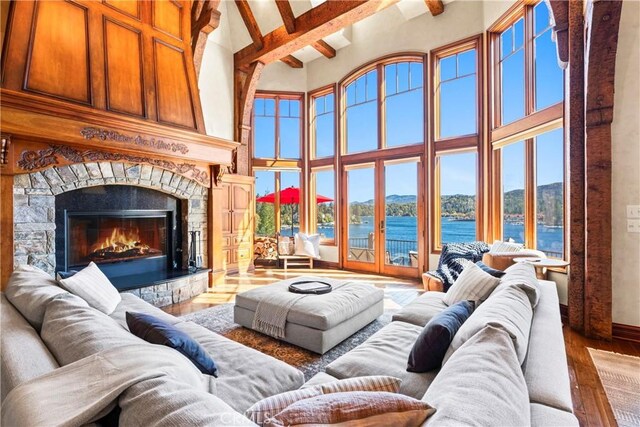 living room featuring wood-type flooring, beamed ceiling, a high ceiling, a stone fireplace, and a water view