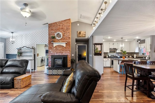 living room with a wood stove, ceiling fan, washer / clothes dryer, wood-type flooring, and lofted ceiling