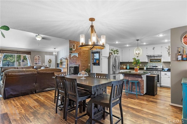 dining space featuring ceiling fan with notable chandelier, light wood-type flooring, a fireplace, and brick wall