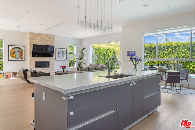 kitchen with a fireplace, a center island with sink, light wood-type flooring, and sink