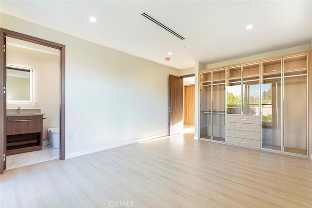 unfurnished bedroom featuring a fireplace, light wood-type flooring, ensuite bathroom, and sink