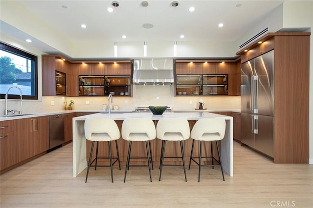 kitchen with sink, wall chimney exhaust hood, an island with sink, a breakfast bar, and appliances with stainless steel finishes