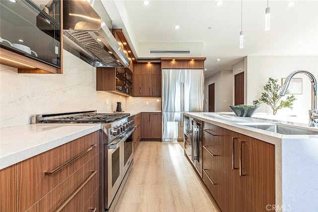 kitchen featuring sink, wall chimney exhaust hood, light hardwood / wood-style flooring, decorative light fixtures, and high quality appliances