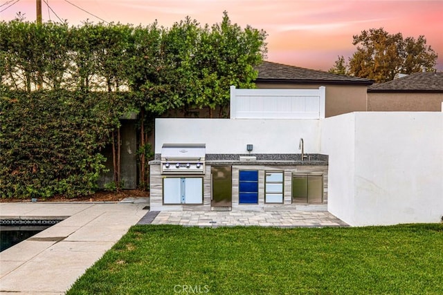 patio terrace at dusk featuring a lawn, area for grilling, a grill, and sink