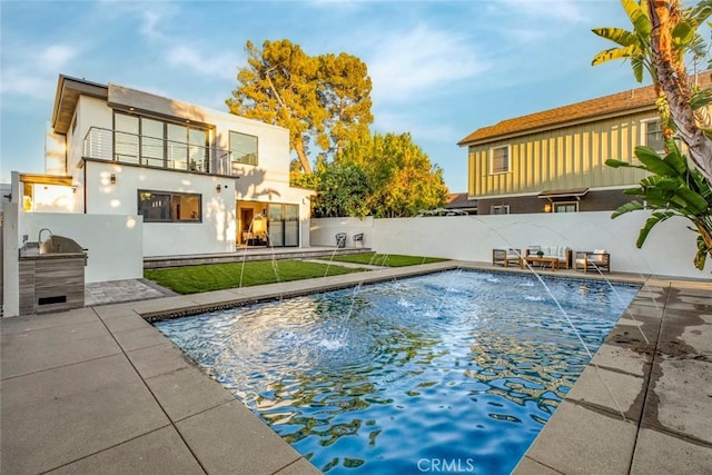 view of pool with pool water feature, a patio, and exterior kitchen