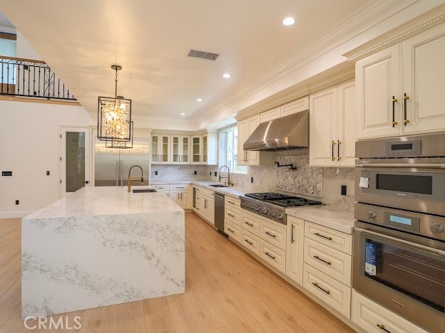 kitchen featuring hanging light fixtures, a kitchen island with sink, light wood-type flooring, and range hood