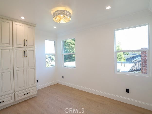 unfurnished bedroom with light wood-type flooring, crown molding, and multiple windows