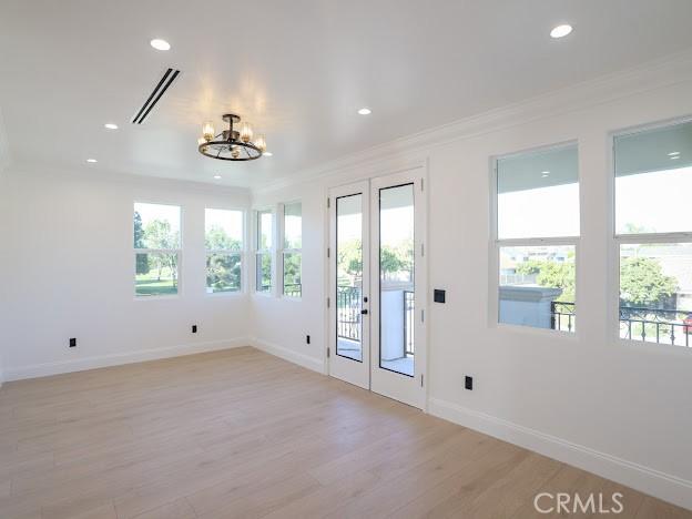 doorway to outside featuring light wood-type flooring, a notable chandelier, and crown molding