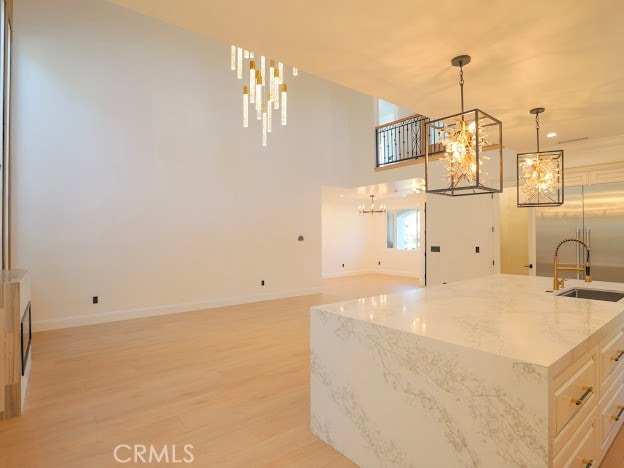 kitchen featuring a kitchen island with sink, light wood-type flooring, sink, light stone countertops, and hanging light fixtures