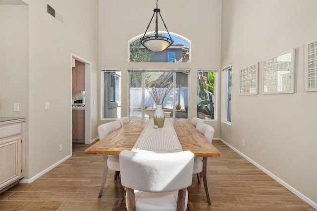 dining room with light hardwood / wood-style floors and a towering ceiling