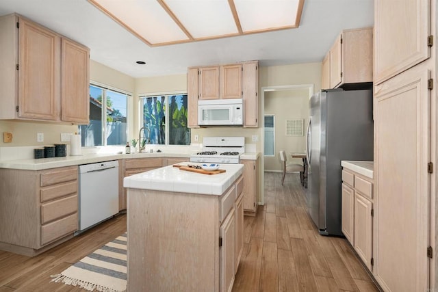 kitchen with white appliances, sink, a kitchen island, light brown cabinetry, and light hardwood / wood-style floors