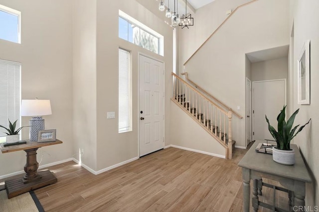 entryway with a high ceiling, light wood-type flooring, an inviting chandelier, and a wealth of natural light