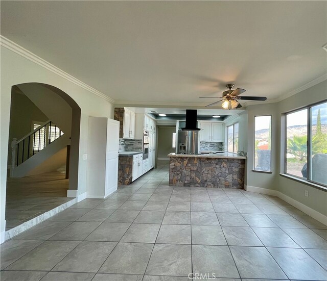 interior space featuring ornamental molding, exhaust hood, white cabinets, and backsplash