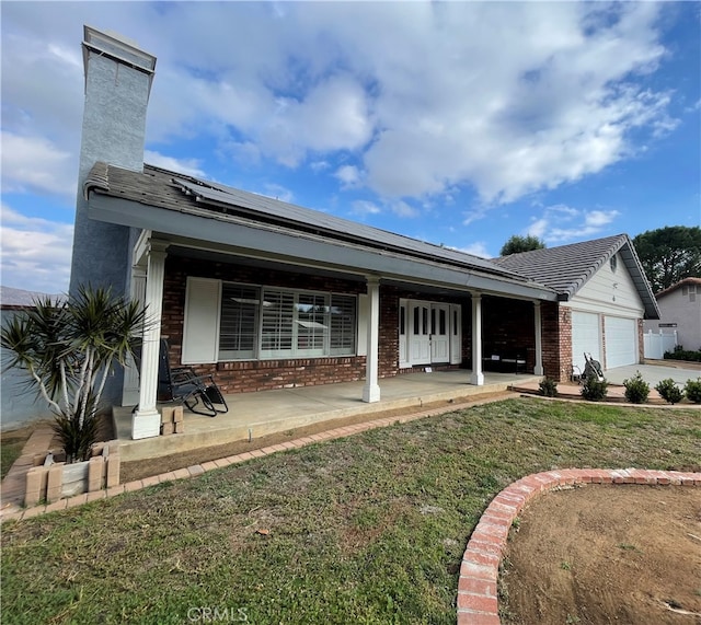 view of front facade featuring a porch, solar panels, a front lawn, and a garage