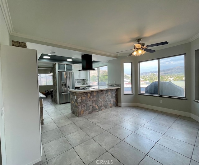 kitchen featuring wall chimney exhaust hood, kitchen peninsula, ornamental molding, stainless steel fridge with ice dispenser, and ceiling fan