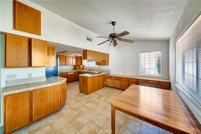 kitchen with ceiling fan, vaulted ceiling, kitchen peninsula, light tile patterned floors, and a textured ceiling