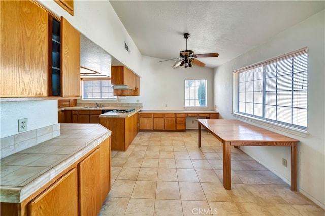 kitchen featuring ceiling fan, gas cooktop, a textured ceiling, and tile counters