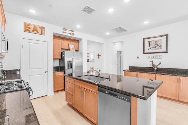 kitchen with appliances with stainless steel finishes, a kitchen island with sink, sink, and dark stone counters