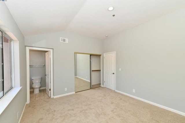 unfurnished bedroom featuring vaulted ceiling, light colored carpet, a closet, and ensuite bath