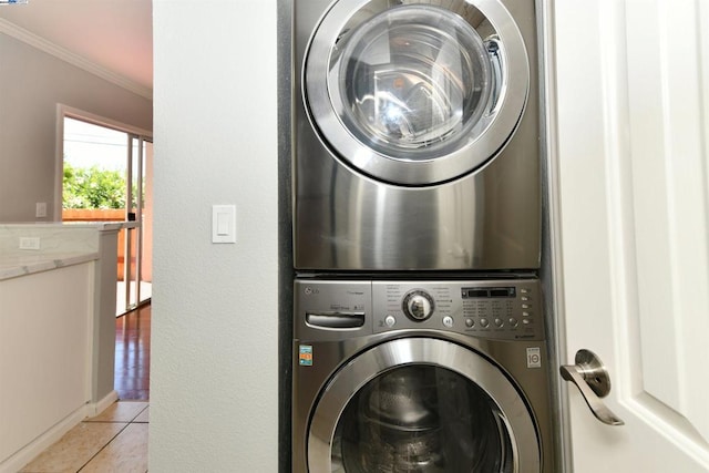 clothes washing area with light tile patterned floors, stacked washer and dryer, and ornamental molding