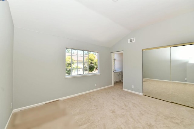 unfurnished bedroom featuring ensuite bath, vaulted ceiling, light colored carpet, and a closet