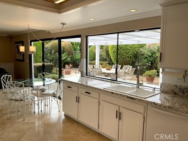 kitchen featuring light stone countertops, white cabinets, decorative light fixtures, and sink