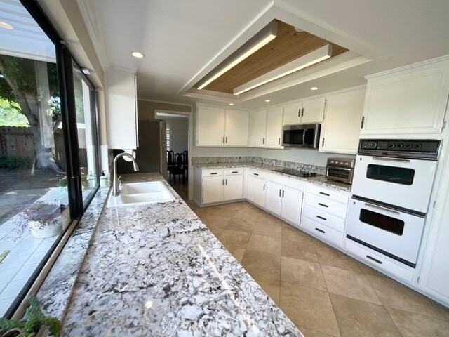 kitchen featuring light stone countertops, white double oven, sink, and white cabinetry