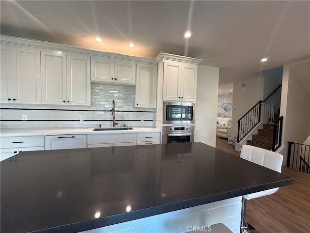 kitchen with oven, white cabinets, sink, and hardwood / wood-style flooring