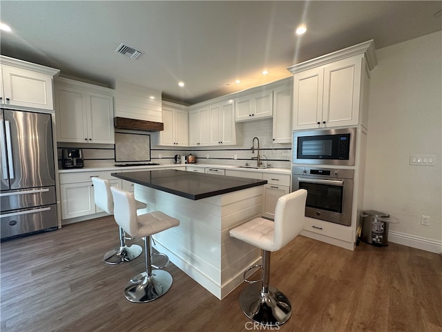 kitchen featuring dark wood-type flooring, sink, stainless steel appliances, white cabinets, and a kitchen bar