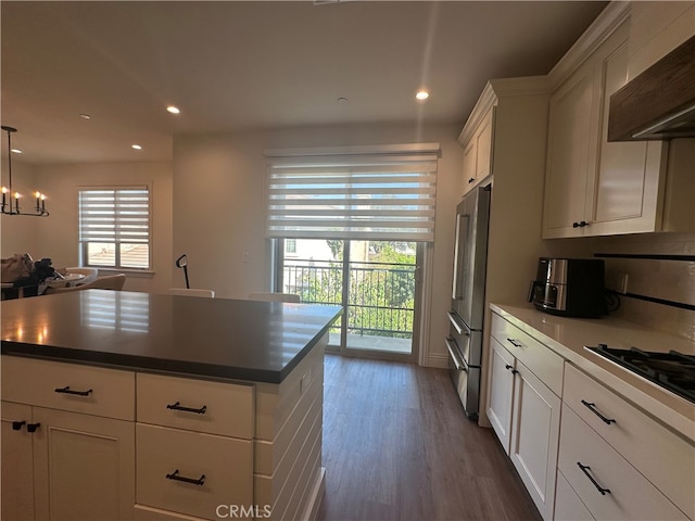 kitchen featuring wall chimney exhaust hood, an inviting chandelier, pendant lighting, dark wood-type flooring, and white cabinets