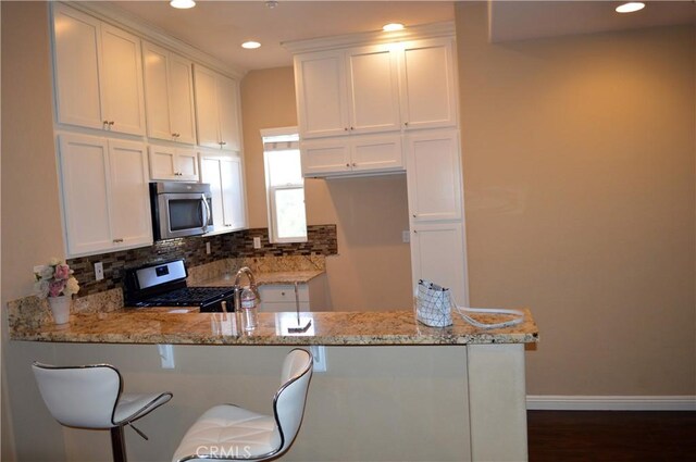 kitchen with kitchen peninsula, light stone countertops, white cabinets, and black range with electric cooktop