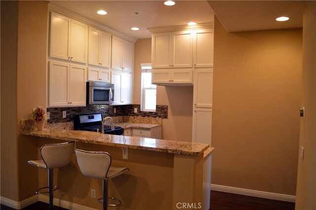 kitchen with light stone countertops, stainless steel appliances, tasteful backsplash, kitchen peninsula, and white cabinets