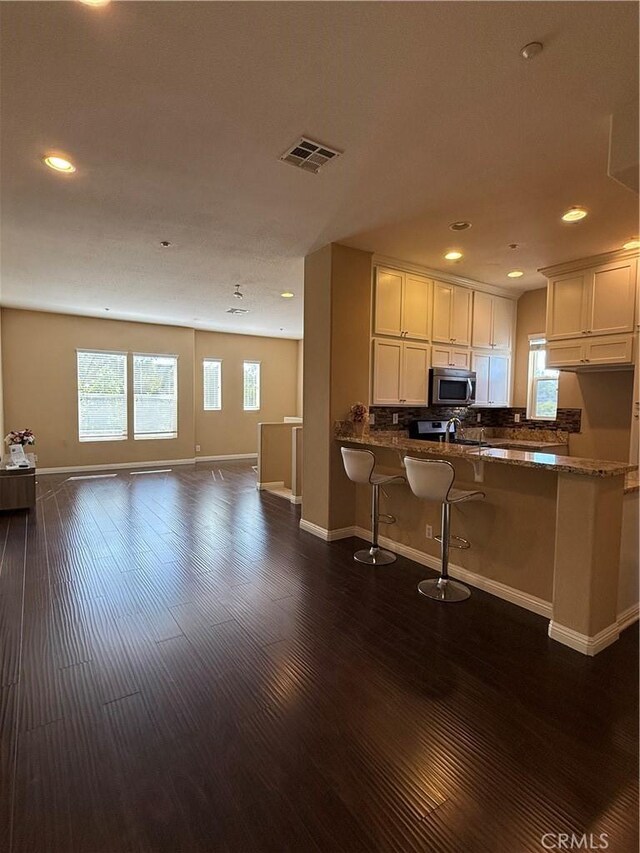 kitchen with stone counters, dark hardwood / wood-style flooring, kitchen peninsula, a kitchen bar, and white cabinets