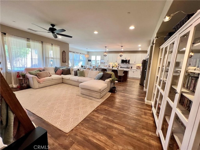 living room featuring ceiling fan with notable chandelier, hardwood / wood-style floors, and sink