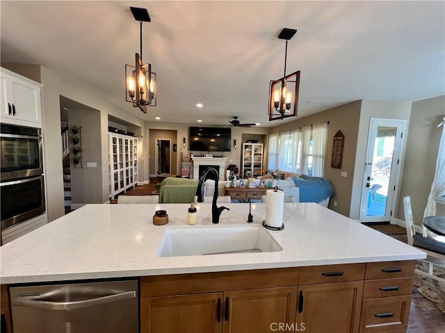 kitchen featuring ceiling fan with notable chandelier, white cabinets, decorative light fixtures, sink, and a center island with sink