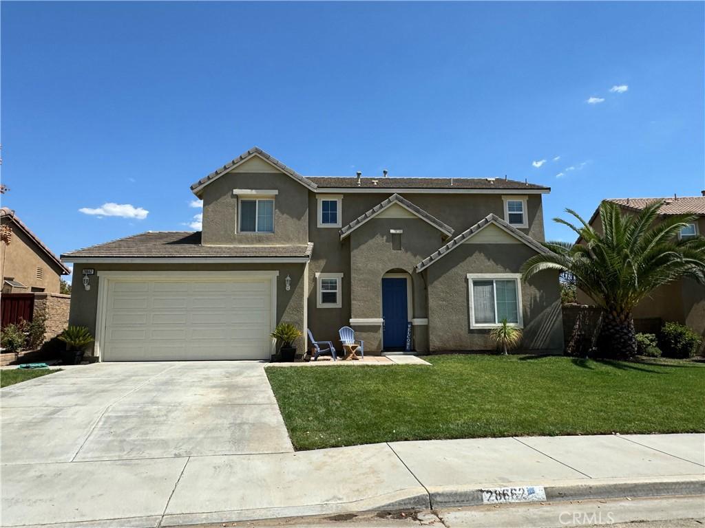 traditional home with a garage, concrete driveway, a front lawn, and stucco siding