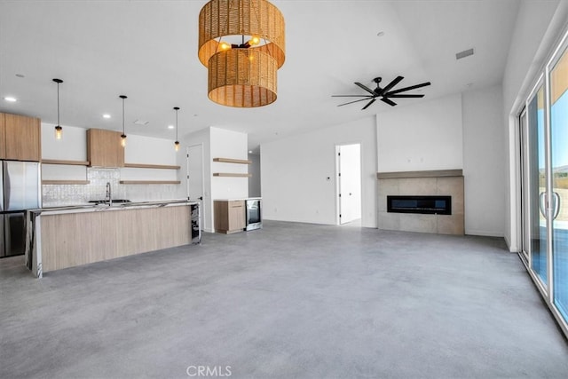 unfurnished living room featuring concrete floors, sink, a tile fireplace, and ceiling fan