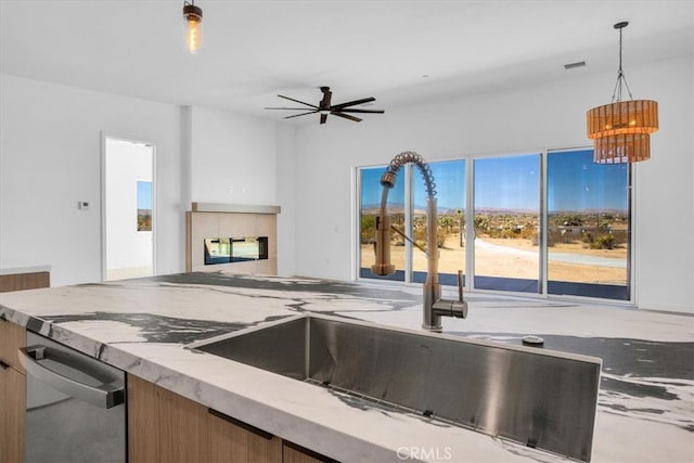 kitchen with light stone counters, ceiling fan, stainless steel dishwasher, sink, and decorative light fixtures