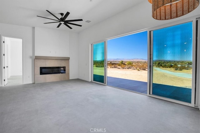 unfurnished living room with a tiled fireplace and ceiling fan