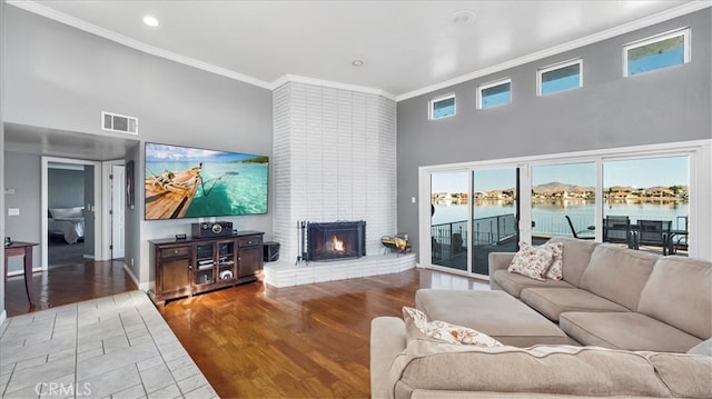 living room featuring a brick fireplace, ornamental molding, hardwood / wood-style floors, and a high ceiling