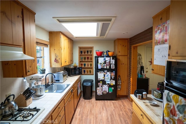 kitchen featuring sink, black appliances, light hardwood / wood-style flooring, and tile counters