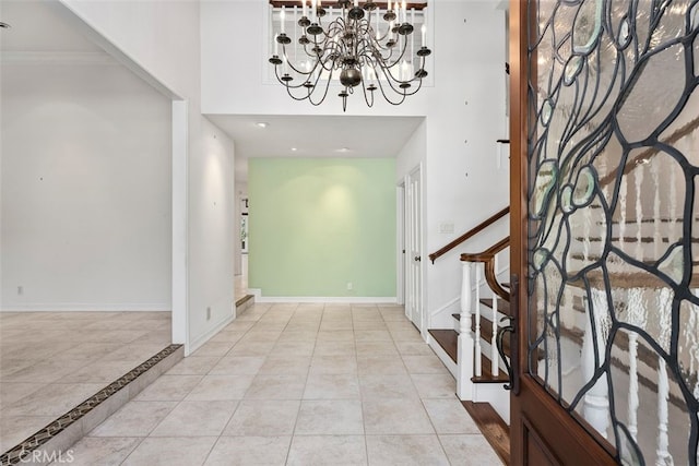 tiled foyer entrance with a notable chandelier, ornamental molding, and a towering ceiling