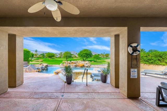 view of patio featuring an in ground hot tub, a mountain view, and ceiling fan