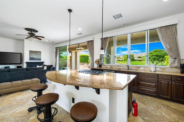 kitchen with a breakfast bar area, light stone countertops, hanging light fixtures, and stainless steel gas cooktop