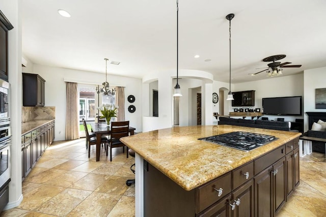 kitchen with light stone counters, dark brown cabinetry, hanging light fixtures, a kitchen island, and appliances with stainless steel finishes