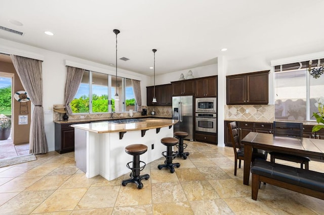 kitchen with decorative backsplash, pendant lighting, a kitchen island, stainless steel appliances, and a kitchen bar