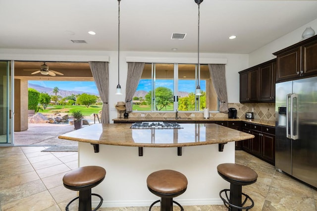 kitchen with decorative backsplash, sink, hanging light fixtures, a breakfast bar area, and stainless steel refrigerator with ice dispenser